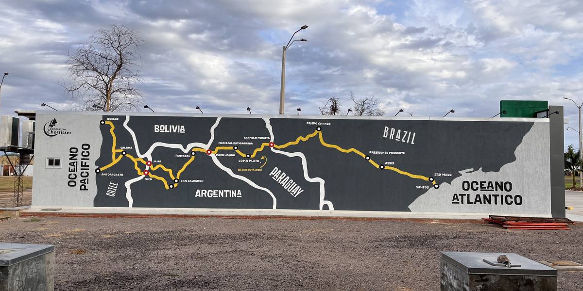 A long roadside mural painting the Bioceanic corridor across Chile, Argentina, Bolivia, Paraguay and Brazil, from the Pacific to the Atlantic, with a marker reading “usted está aquí” beside Loma Plata.